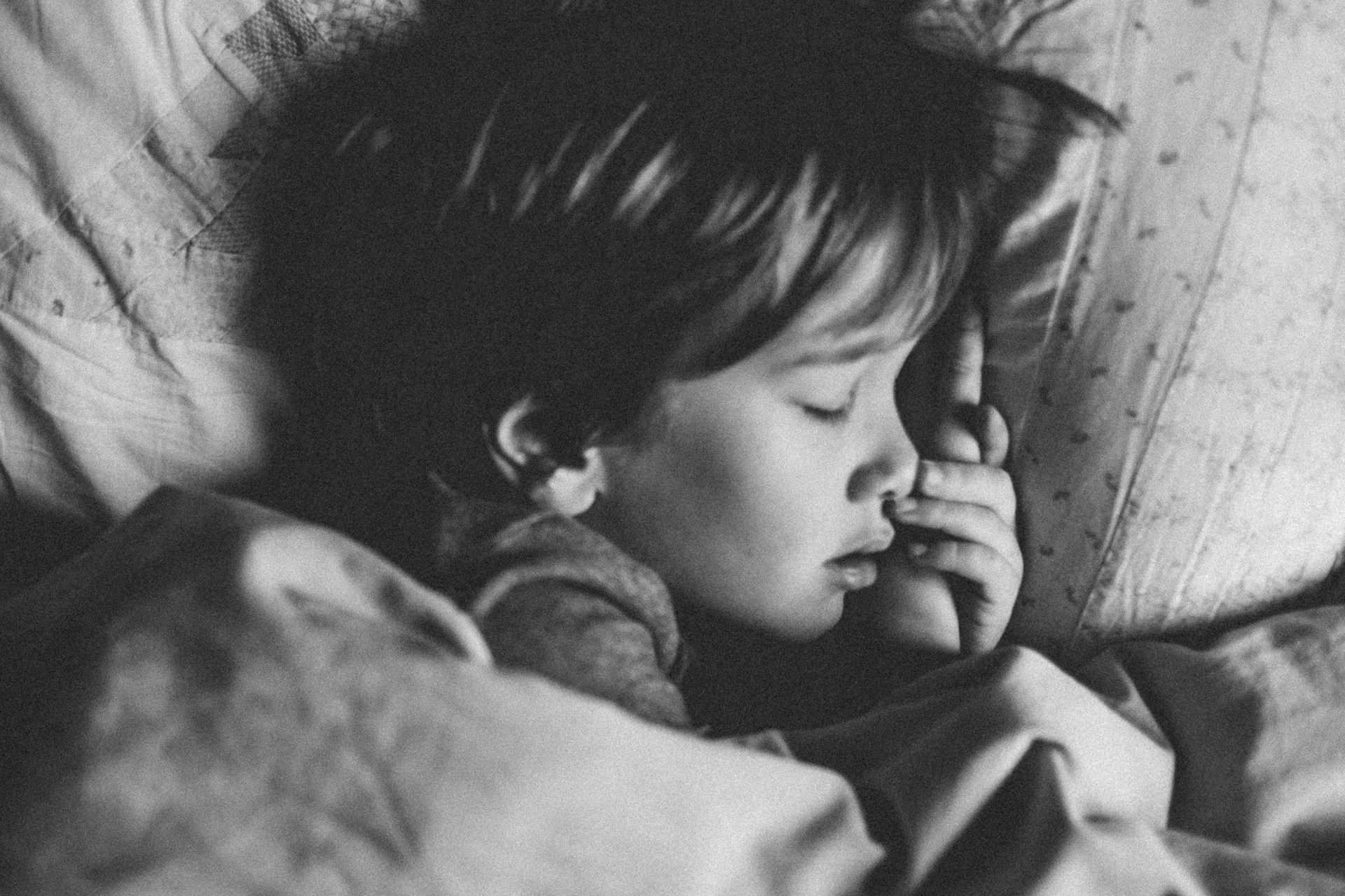 Black and white photograph of a young child peacefully sleeping, with a serene expression on their face. The child is nestled in blankets, embodying a sense of innocence and calm.