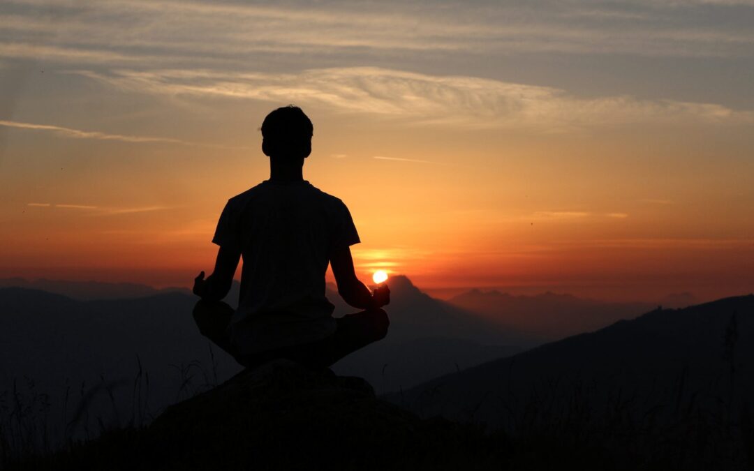 Person in silhouette sitting before a sunset over mountains