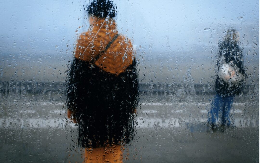 Person standing alone seen through a rain-covered window