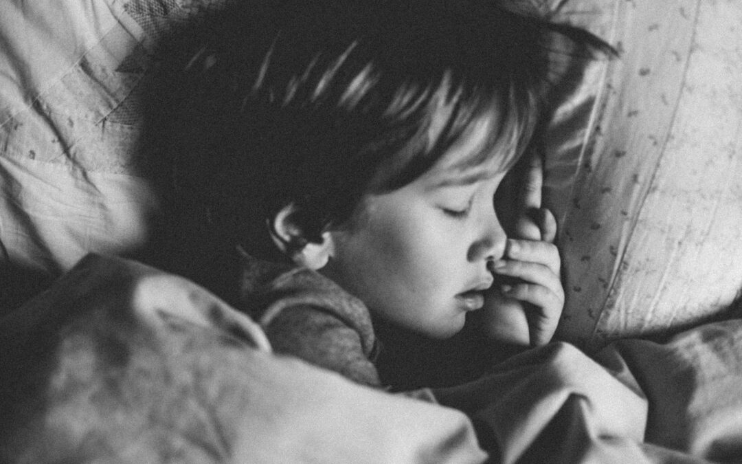 Black and white photograph of a young child peacefully sleeping, with a serene expression on their face. The child is nestled in blankets, embodying a sense of innocence and calm.