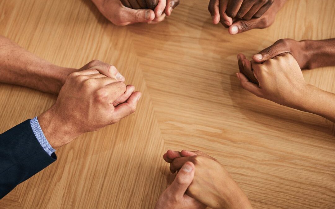 People holding hands in a circle over a wooden table