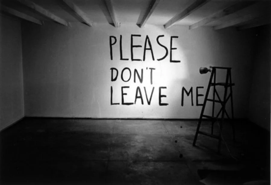 Black and white photo of a wall painted with the words Please don't leave me